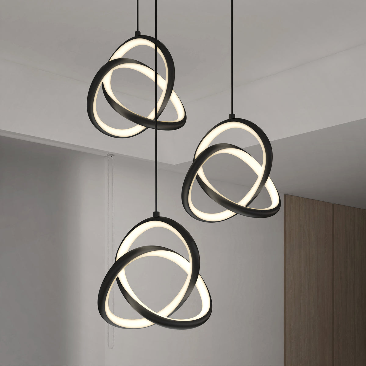 Three modern pendant lights with intertwined, glowing LED rings hang from the ceiling in a minimalist room with white walls and a wooden accent.