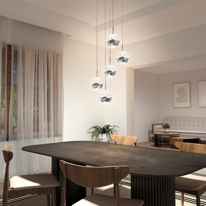 A modern dining room with a dark wooden table, four wooden chairs, and the Artika-CAN-dev Oracle modern 5-light LED pendant hanging above. Sunlight filters through sheer curtains, with a cozy living area visible in the background.