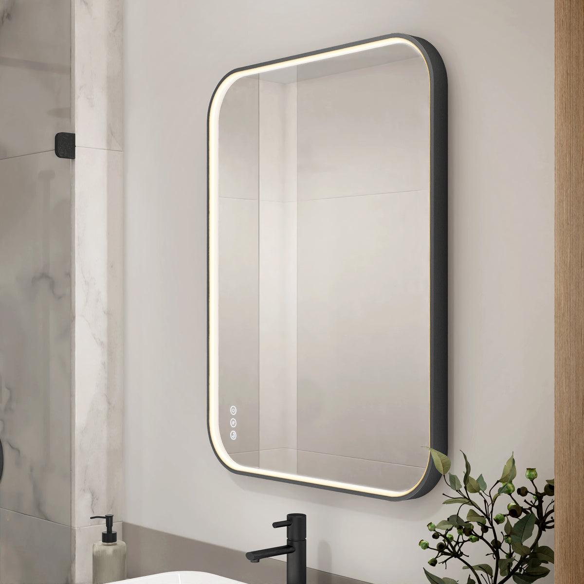 The Artika Royce Dimmable LED Mirror, 3 CCT, is mounted above a sink with a black faucet. It features adjustable colour temperature and a built-in defogger. A plant and soap dispenser are nearby. Can be installed horizontally or vertically.