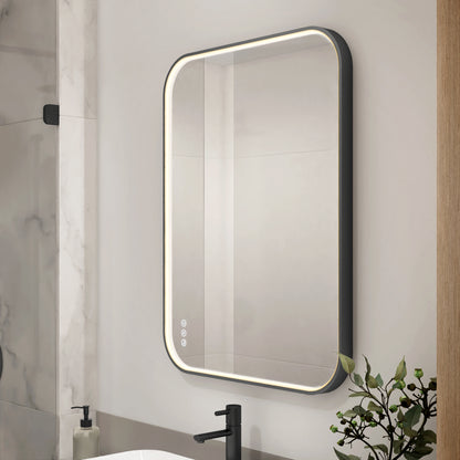 The Artika Royce dimmable LED mirror 3 CCT is a modern rectangular bathroom mirror with rounded corners, touch controls, and integrated edge lighting, shown above a white sink with black faucet and nearby soap dispenser.