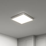 A modern, square-shaped ceiling light fixture with rounded edges emits a bright, even glow in a minimalist room with white walls and cabinets.
