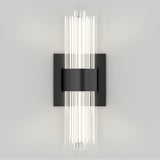 A modern wall sconce with vertical cylindrical glass rods emitting soft white light, mounted on a rectangular black metal base against a plain light-colored wall.