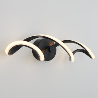 The Artika Swirl LED bathroom vanity light features three curved black arms with integrated LEDs, mounted on a round black base for a soft white glow against a light gray wall.
