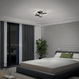 A modern bedroom with a large bed, gray and white bedding, green accent pillows, a potted plant, floor-to-ceiling windows with city view, and a contemporary ceiling light fixture.