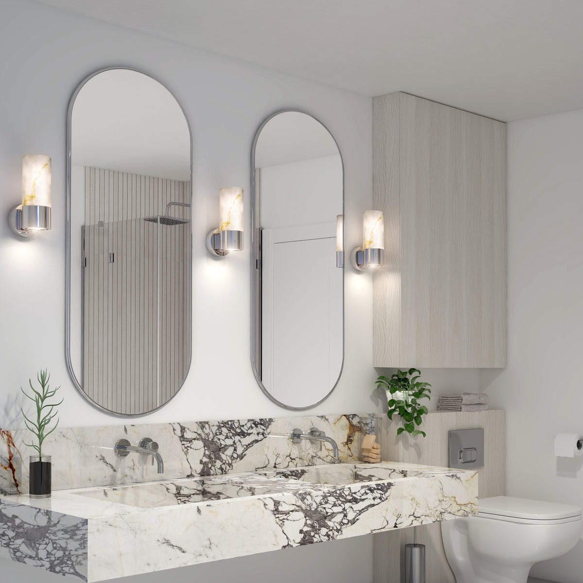 Modern bathroom with two oval mirrors above a marble countertop, wall-mounted sink faucets, two sconces, a toilet, and plants as accents. Light wood cabinets and neutral tones create a clean, elegant look.