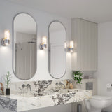 Modern bathroom with two oval mirrors above a marble countertop, wall-mounted sink faucets, two sconces, a toilet, and plants as accents. Light wood cabinets and neutral tones create a clean, elegant look.