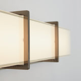 Close-up of a modern wall-mounted rectangular light fixture with frosted glass and metal frame, emitting a soft, warm glow against a light-colored wall.