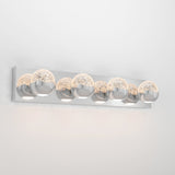A modern wall-mounted light fixture with five spherical glass shades, each containing decorative bubbles. The fixture has a sleek chrome finish and is mounted on a rectangular chrome base against a white wall.