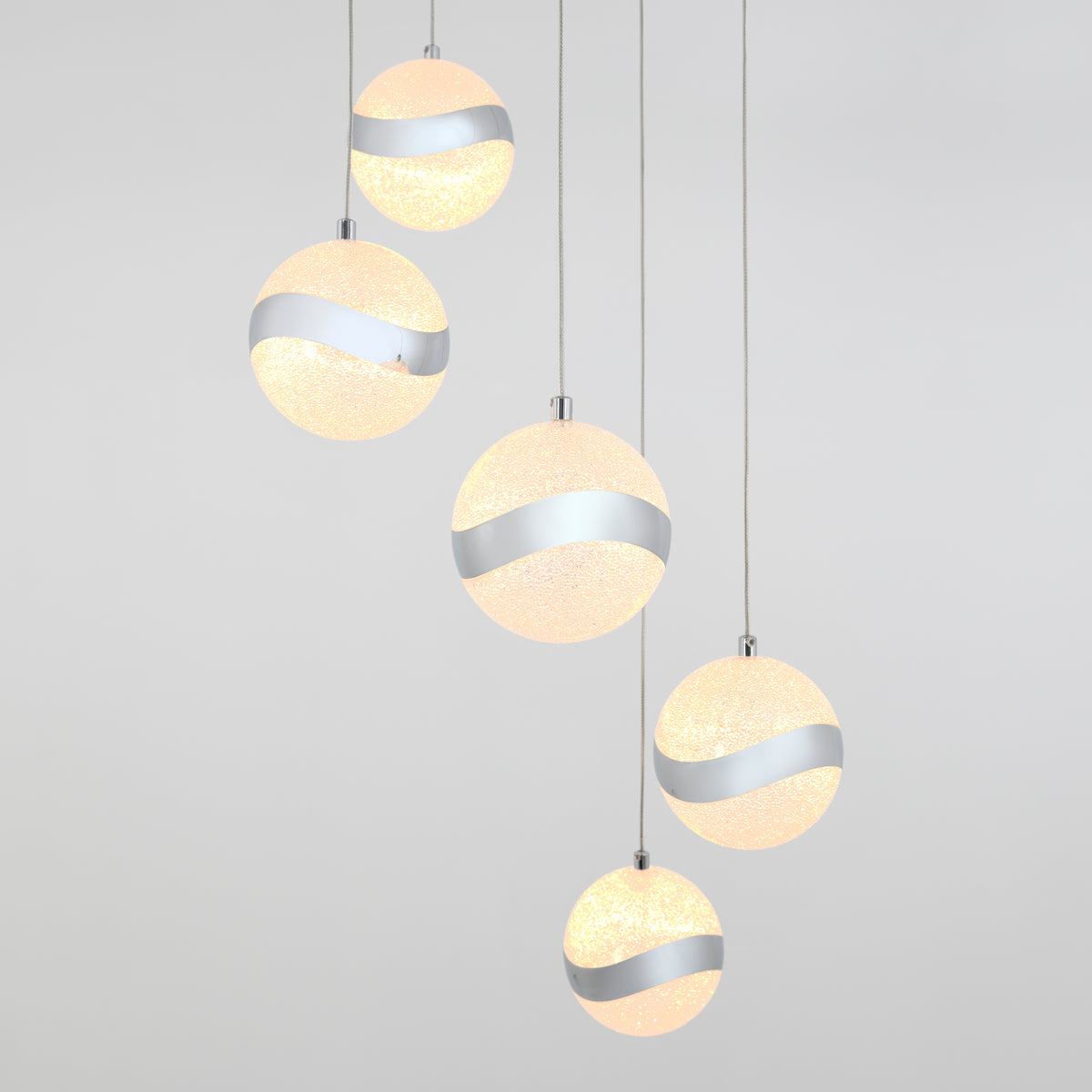 Five spherical pendant lights with sparkly surfaces and a wavy metallic stripe hang at varying heights against a plain light gray background.