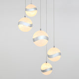 Five spherical pendant lights with sparkly surfaces and a wavy metallic stripe hang at varying heights against a plain light gray background.