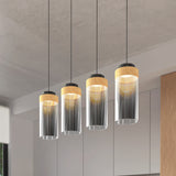 Four modern pendant lights with cylindrical glass shades and golden accents hang in a row from the ceiling in a contemporary room with neutral colors and clean lines.