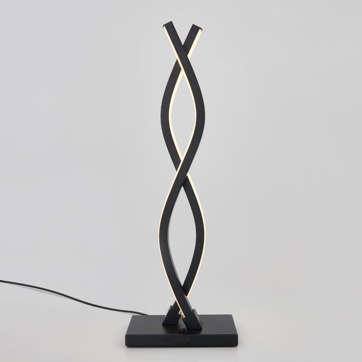 A modern table lamp with two twisting, black metal light strips on a square base, emitting a soft white light. The lamp is plugged in with a visible black cord against a plain light background.