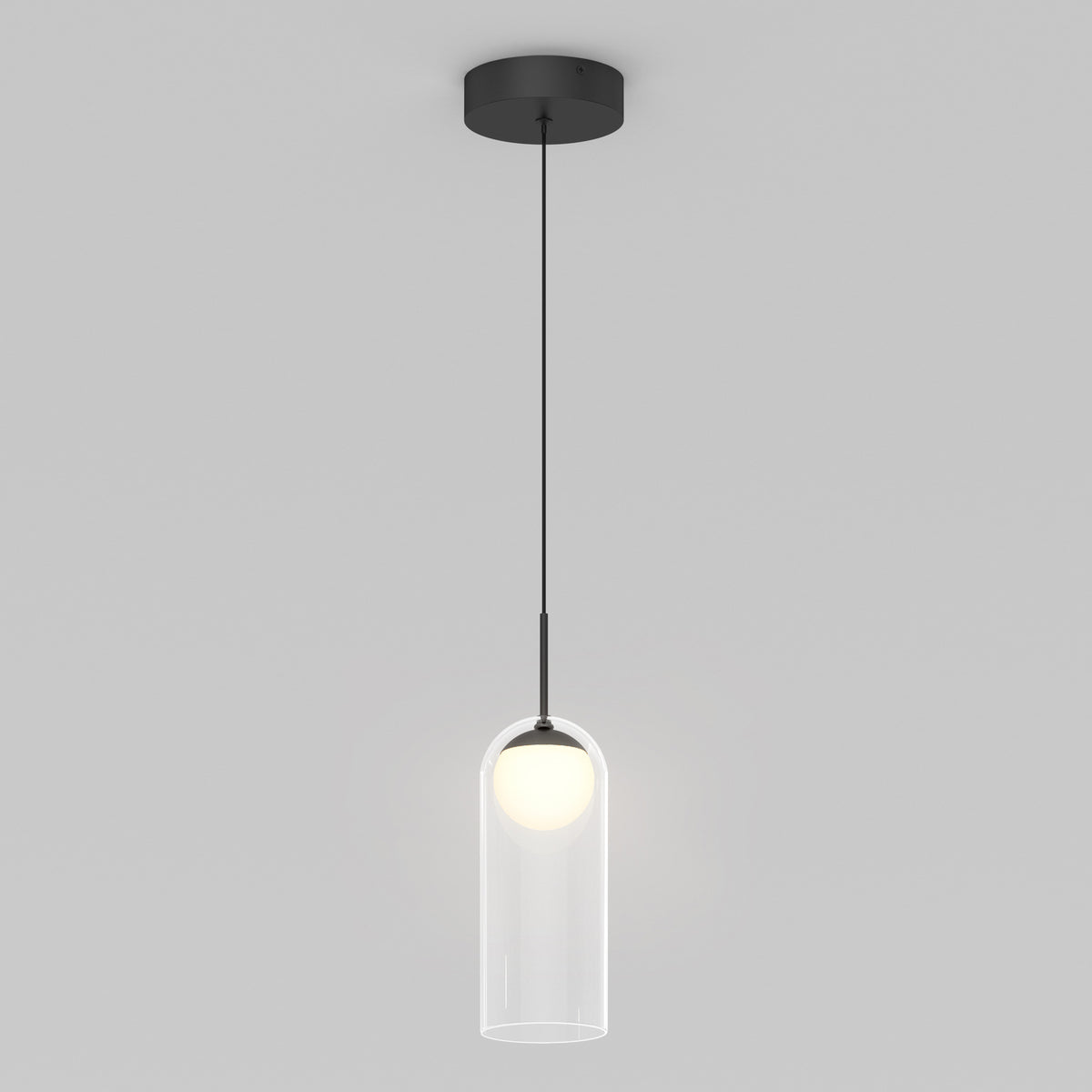 A modern pendant light with a black ceiling mount, thin black cord, and a clear cylindrical glass shade enclosing a glowing round bulb, set against a plain gray background.