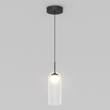 A modern pendant light with a black ceiling mount, thin black cord, and a clear cylindrical glass shade enclosing a glowing round bulb, set against a plain gray background.