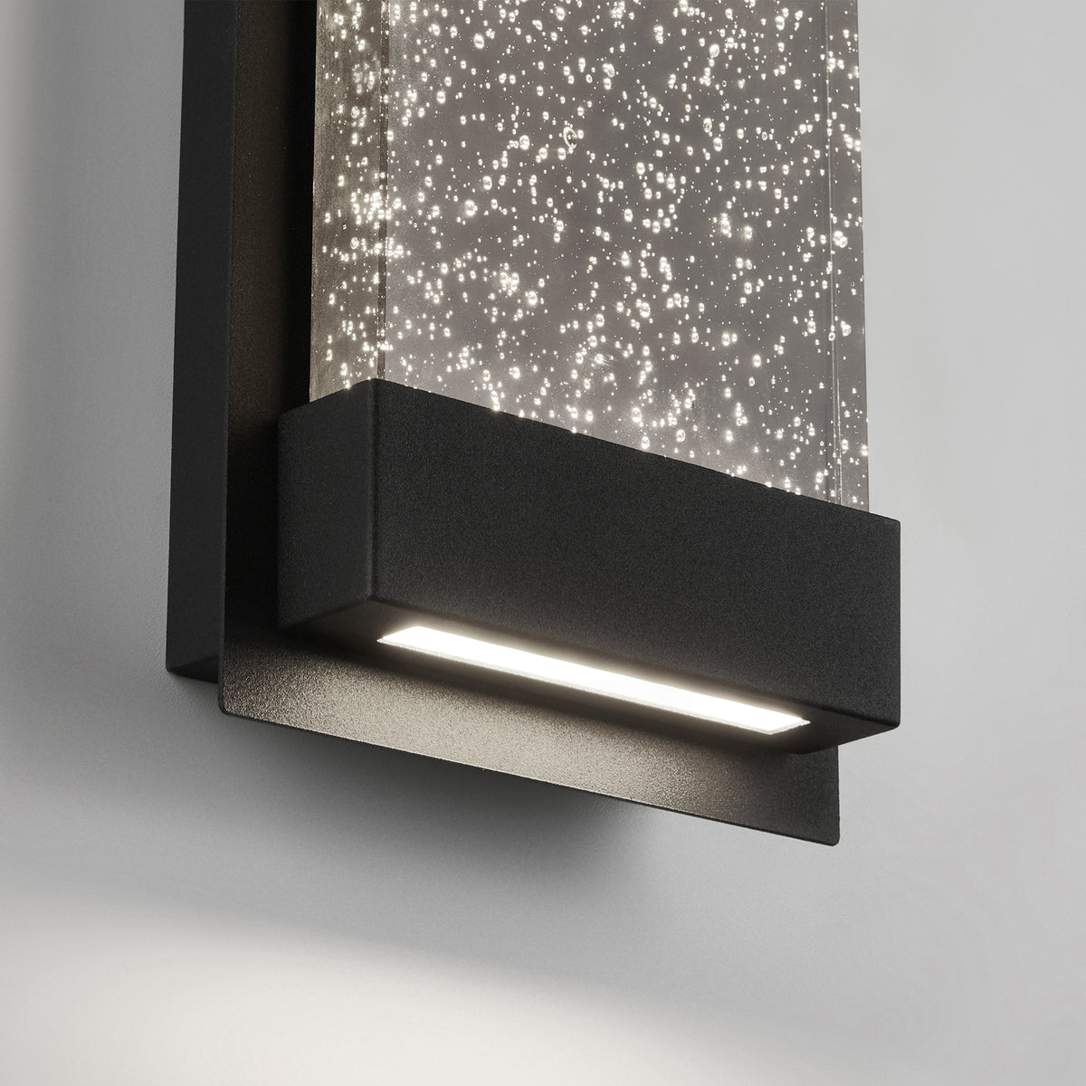 Close-up of the Artika Essence Glow Box indoor-outdoor LED wall light, featuring a black frame and a rectangular panel with tiny illuminated bubbles that create a sparkling effect against a white background.