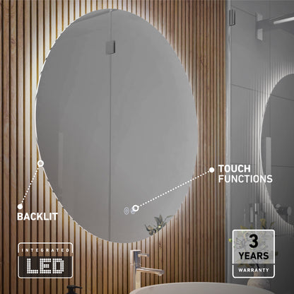 The Artika Raya 24 in. oval LED mirror with 3 CCT and defogger is mounted on a wooden slat wall. It features touch controls, integrated lighting, and a visible sink below. A label indicates a 3-year warranty.