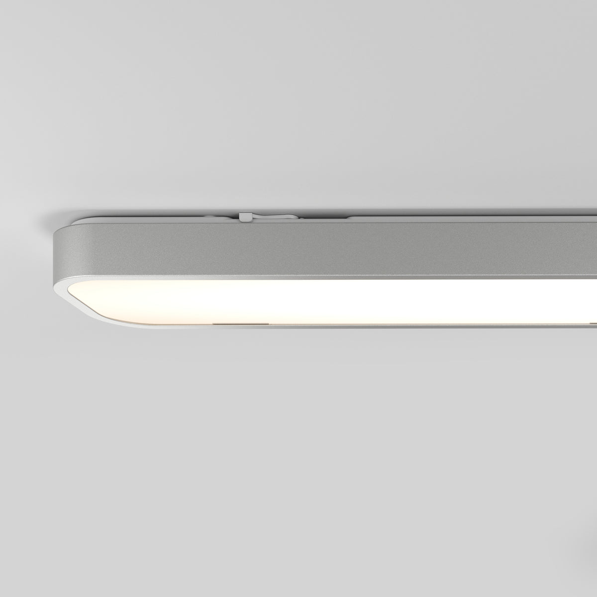 A close-up view of a modern, rectangular ceiling light fixture with rounded edges, emitting a soft white glow against a plain, light gray ceiling.