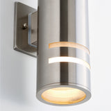 A modern wall-mounted cylindrical stainless steel light fixture with horizontal cut-out slits allowing light to shine through, and a frosted circular glass cover on the bottom, attached to a square wall plate.