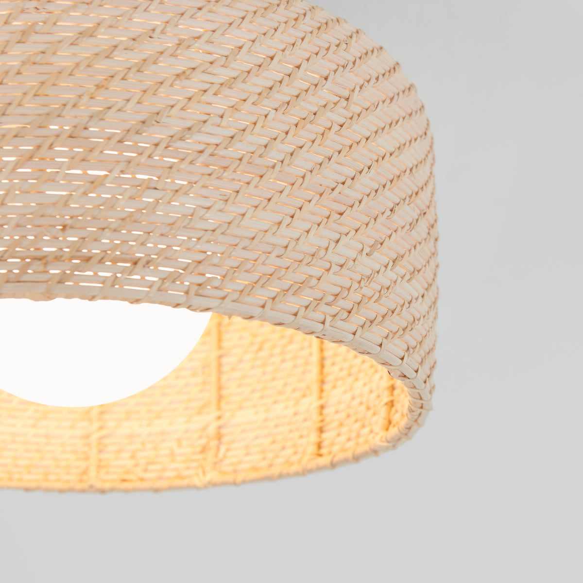 Close-up of the Emiko modern LED flush mount light 5 CCT by Artika, featuring a woven light rattan shade and a bright white bulb glowing inside, set against a plain, light background.