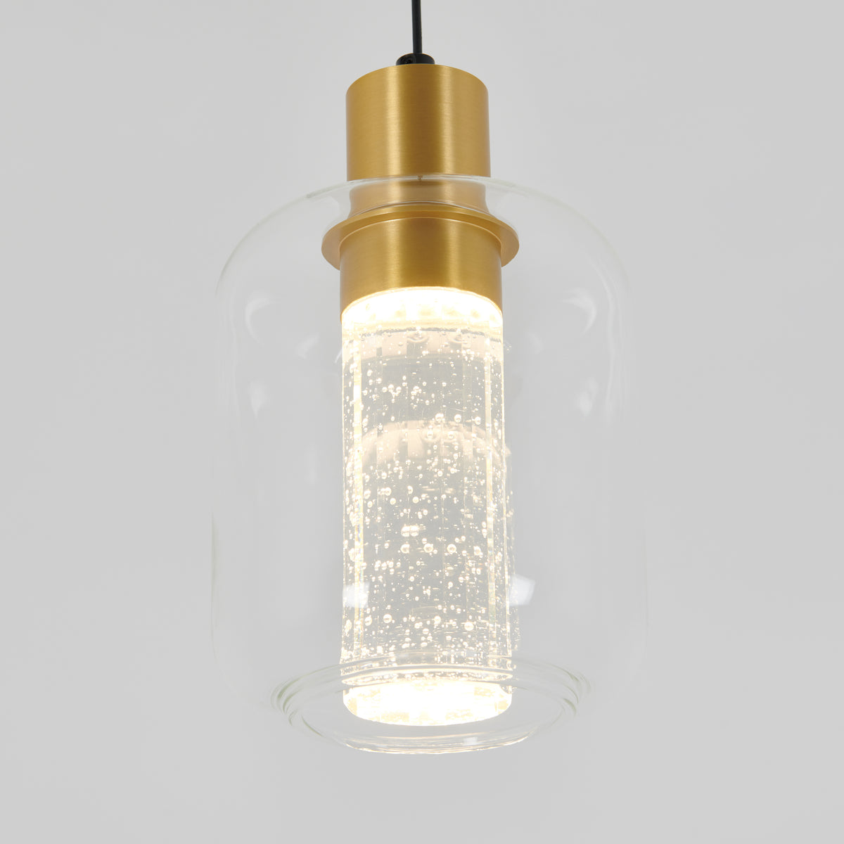 A modern pendant light with a clear glass shade, a cylindrical inner diffuser filled with bubbles, and gold metal accents, suspended by a black cord against a plain light background.