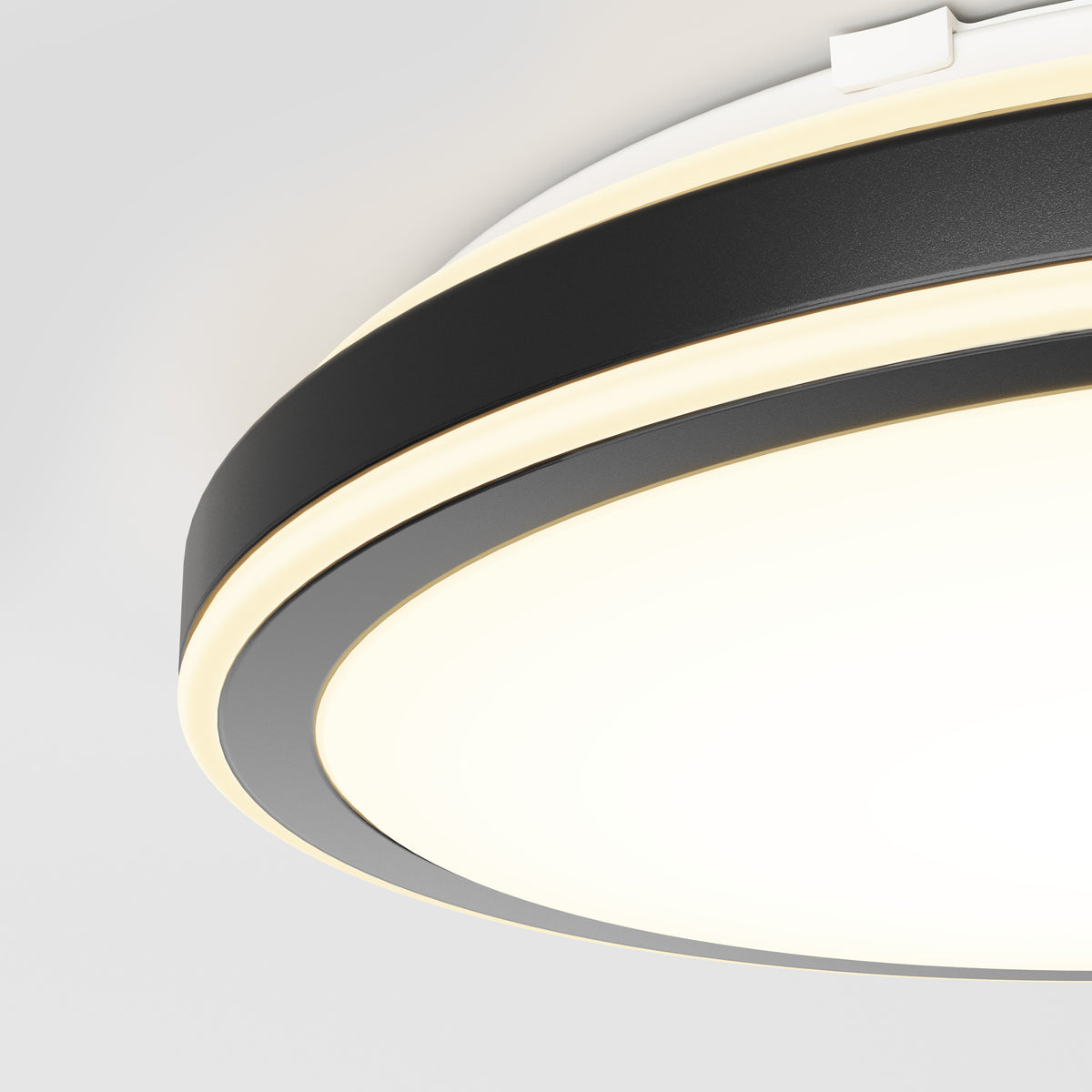 A close-up view of a modern ceiling light fixture with circular, black and white bands and a glowing, diffused light, mounted on a white ceiling.