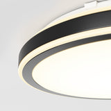 A close-up view of a modern ceiling light fixture with circular, black and white bands and a glowing, diffused light, mounted on a white ceiling.