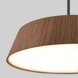 Close-up of a modern pendant light with a circular wood-textured lampshade and a glowing white diffuser, hanging from a black cord against a plain light gray background.