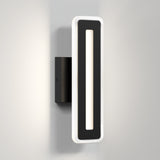 A modern black wall sconce with a rectangular design, featuring a central cutout and a white illuminated border, mounted on a light gray wall.