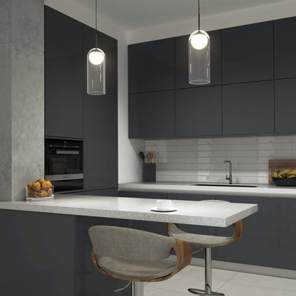 Modern kitchen with dark cabinets, light gray countertop, barstool, bowl of oranges, minimalist decor, and a cup and saucer on the counter. The space features the Mirah LED modern mid-century pendant light 3 CCT by Artika.