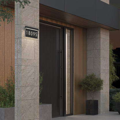 Modern house entrance with a vertical black door, light stone walls, wooden paneling, large potted plants, and an Artika Bowen Modern LED Outdoor Address Wall Light 5 CCT displaying the number 18095.