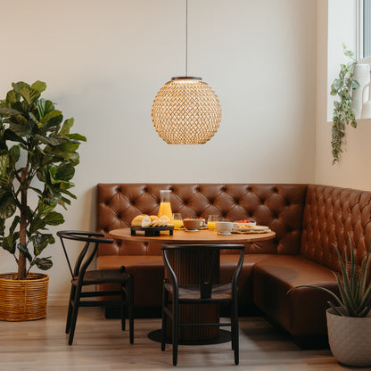 A cozy dining nook features a round wooden table, brown tufted leather bench, black chairs, potted plant, and breakfast foods by a window illuminated by the Benson LED pendant light 5 CCT from Artika.