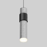 A modern cylindrical pendant light with a speckled concrete finish, black metal accent band, and a glowing white bottom, suspended by a thin black cord against a plain gray background.