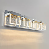 A modern wall-mounted light fixture with four rectangular LED lights, featuring clear panels with sparkling bubble details, emits a warm glow onto a white wall.