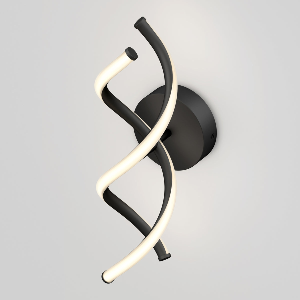 A modern wall light fixture featuring two intertwined, spiral tubes—one illuminated and white, the other black—mounted on a round black base against a plain light gray background.