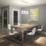 Modern dining room with a wooden table, four white chairs, a black and white patterned rug, a vase with yellow flowers, large abstract artwork, and pendant lights. Window and glass door reveal greenery outside.