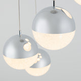 Three modern spherical pendant lights with a metallic upper half and a textured, glowing lower half hang against a light gray background, creating a sleek and contemporary look.