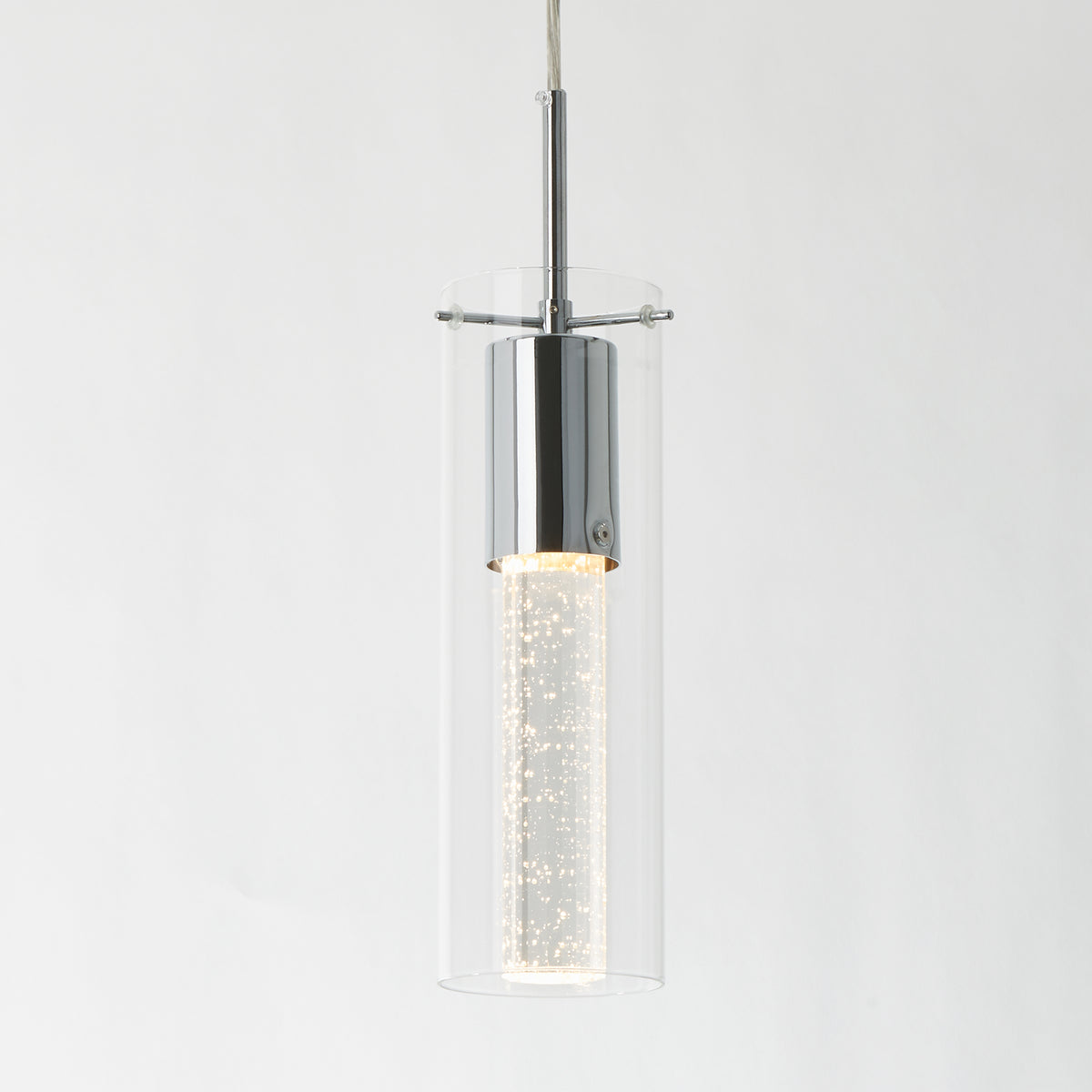 A modern pendant light with a cylindrical clear glass shade and chrome fixture, featuring a bubble-filled illuminated center, hangs against a plain white background.