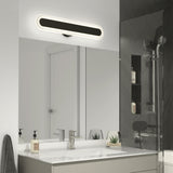 Modern bathroom with a rectangular mirror, white sink, and silver faucet. Above the mirror is an elongated, oval light fixture. The countertop holds soap dispensers and small plants; a glass shower is visible to the right.