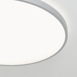 A close-up view of a round ceiling light fixture with a smooth white surface and a thin gray rim, glowing brightly against a plain white ceiling.