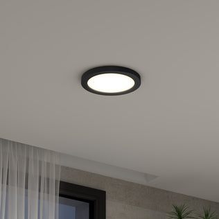 The Artika Europa Disk 7 in. LED modern flush mount light with a black rim is lit on a white ceiling, while sheer-curtained windows and a green plant appear in the image corners.