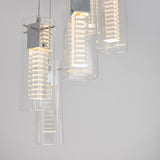 Close-up of modern pendant lights with clear cylindrical glass shades and metal fixtures, softly illuminated against a plain light gray background.