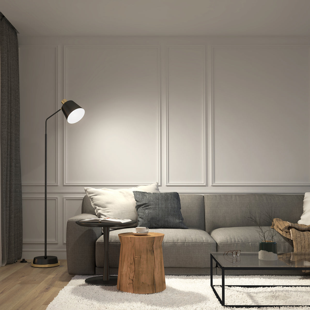 A modern living room with a gray sofa, throw pillows, a floor lamp, small round tables—one wooden and one metal—a glass coffee table, and a light-colored rug on a wooden floor. White paneled walls are in the background.