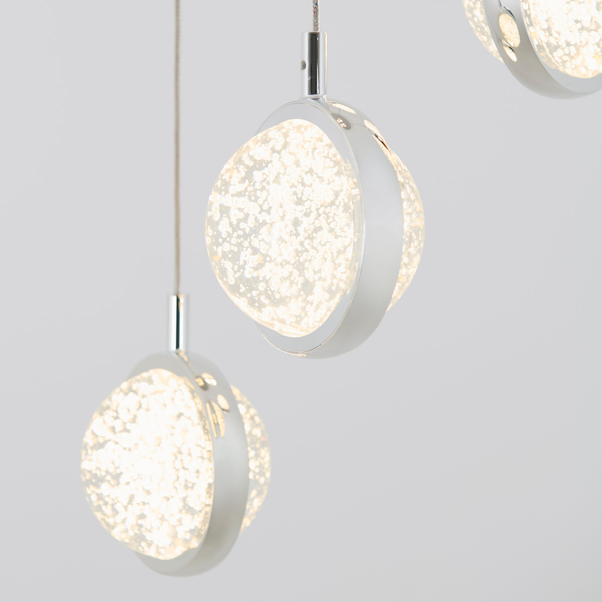 Three modern pendant lights with round, frosted glass shades featuring a speckled pattern, suspended by thin cords against a plain light gray background.