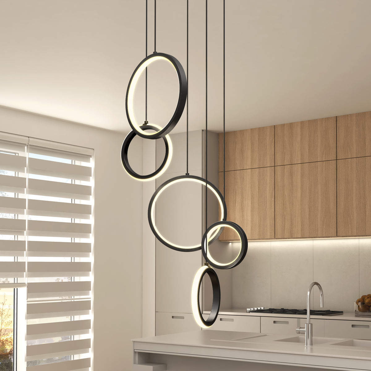 Modern kitchen with light wood cabinets, a white countertop, and a set of four black circular pendant lights hanging at different heights above an island. Window with horizontal blinds lets in natural light.