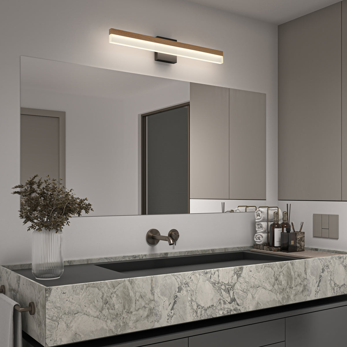 Modern bathroom with a large marble sink, wall-mounted faucet, a wide frameless mirror, a linear LED light above the mirror, beige cabinets, and a vase with dried flowers on the counter.
