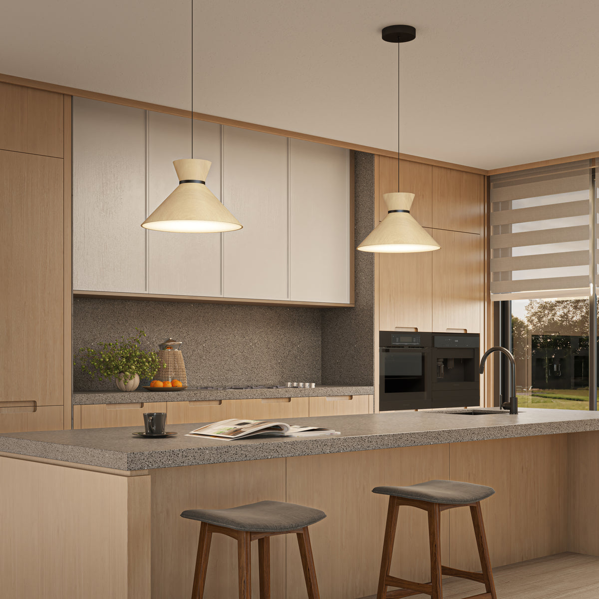 A modern kitchen with light wood cabinets, a gray countertop island, two cushioned stools, pendant lights, built-in appliances, a sink, and a window with a dual-layered roller blind. An open book and fruit are on the island.