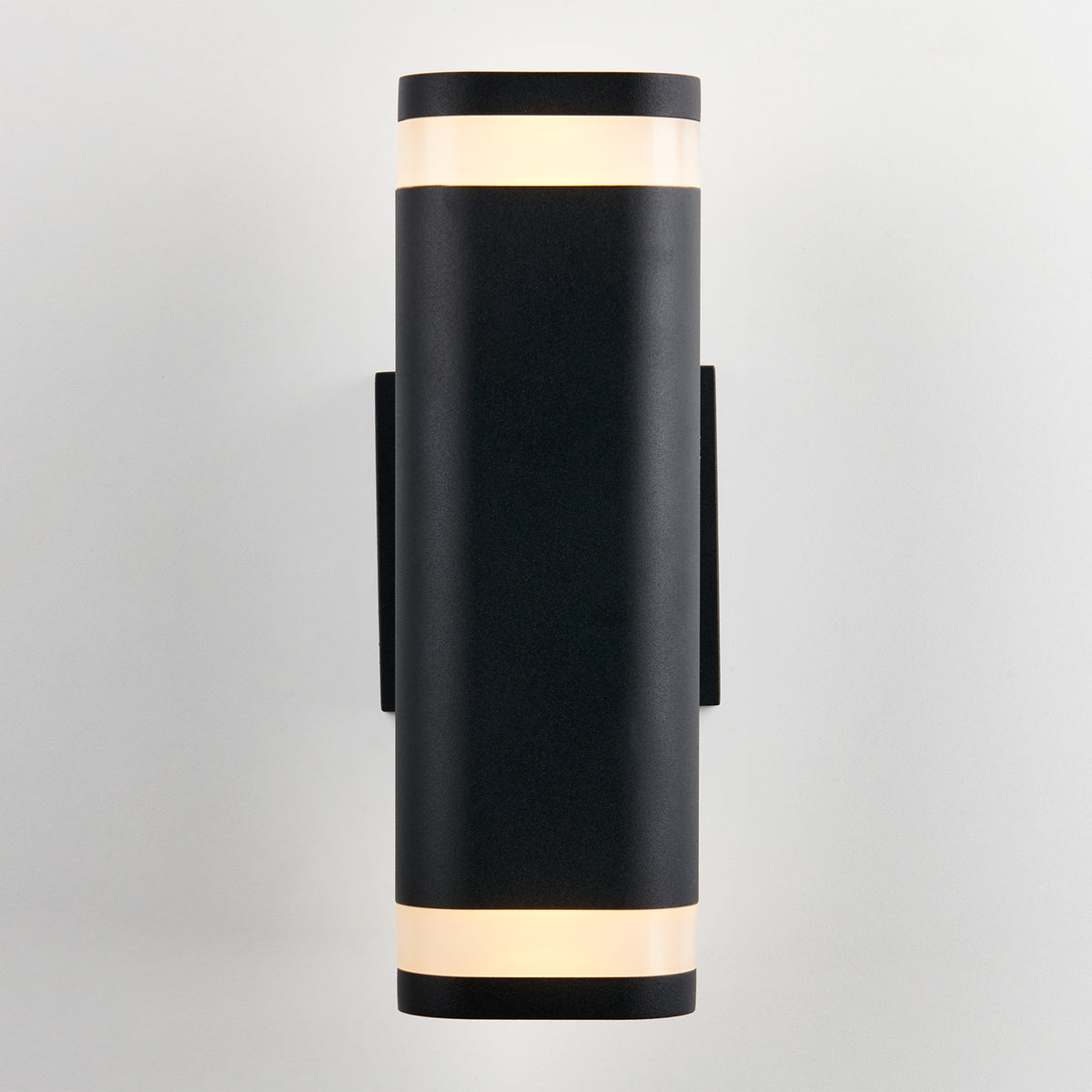 A modern black wall sconce with a cylindrical shape, featuring illuminated frosted bands at the top and bottom, mounted on a light-colored wall.