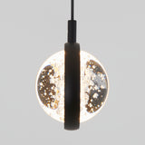 A modern pendant light with a round, illuminated glass globe featuring bubble-like textures, partially obscured by a vertical black metal strip, hanging against a plain light gray background.