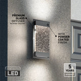 A modern rectangular LED wall light with a textured premium glass diffuser and powder-coated finish is mounted on a gray exterior wall. Text highlights its features and a 5-year warranty.