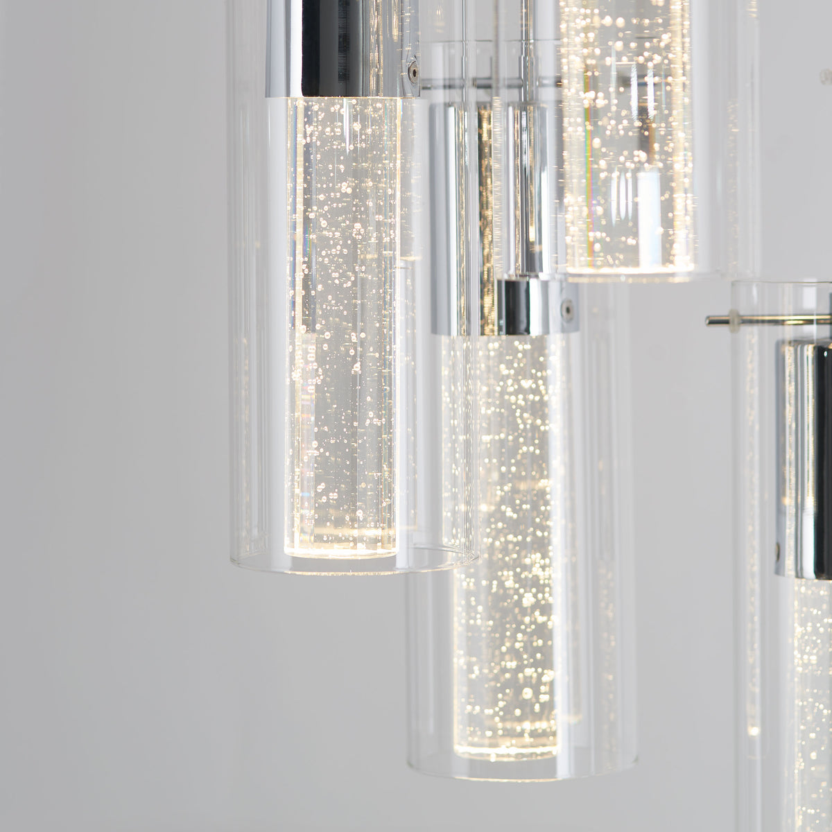 Close-up of modern pendant lights with cylindrical glass covers, featuring tiny bubbles and bright white LED illumination, giving a sparkling effect against a soft grey background.